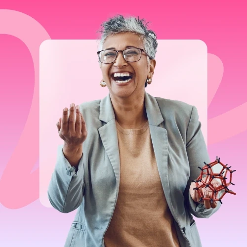A gray-haired woman in glasses and a blazer laughs heartily while holding a red and black molecular model in her left hand.