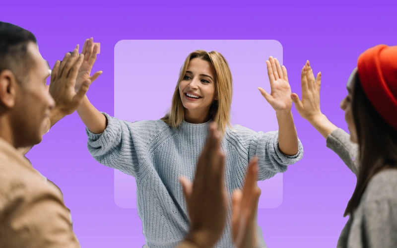 A smiling woman in a light blue sweater extends both hands forward, while other hands appear to be high-fiving her from the sides, all against a purple background.