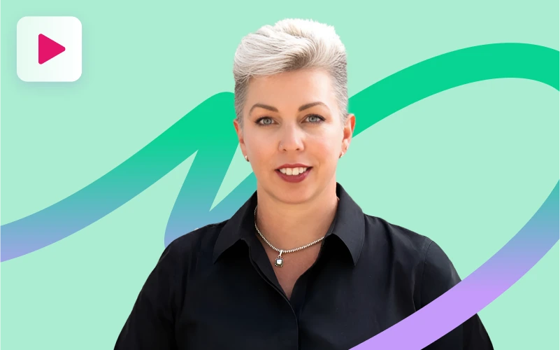 A woman with short, light-colored hair and a black collared shirt smiles slightly at the camera, wearing a silver chain with a heart pendant, against a mint green and purple abstract background with a play button icon.